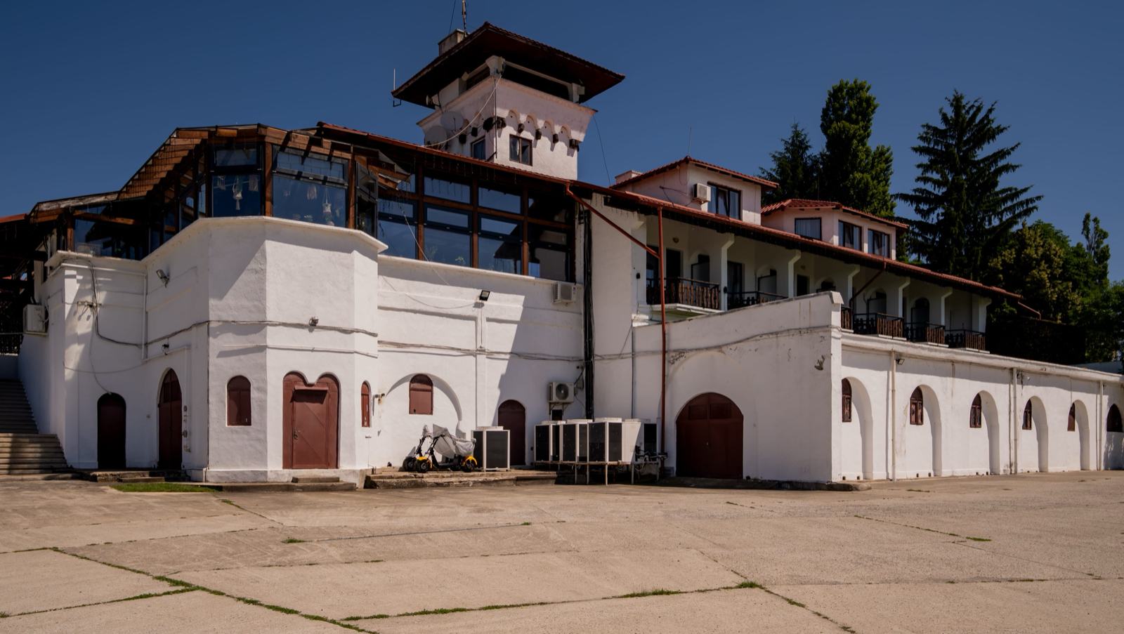 Fațada albă a casei, cu arcade, acoperiș roșu și turnul de deasupra