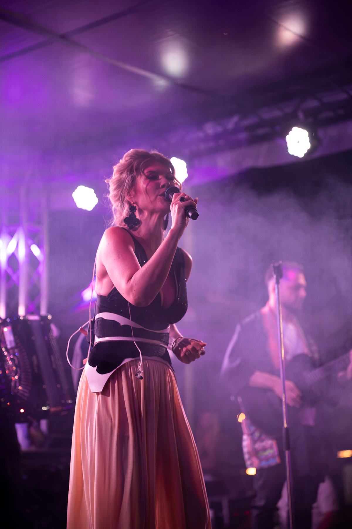 Diana Matei cântând pe scenă, în lumină violet, cu taraful în spate