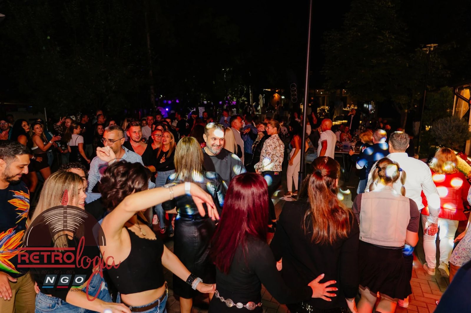Lumea dansând noaptea în curte, sub luminile globului disco, cu mesele în fundal