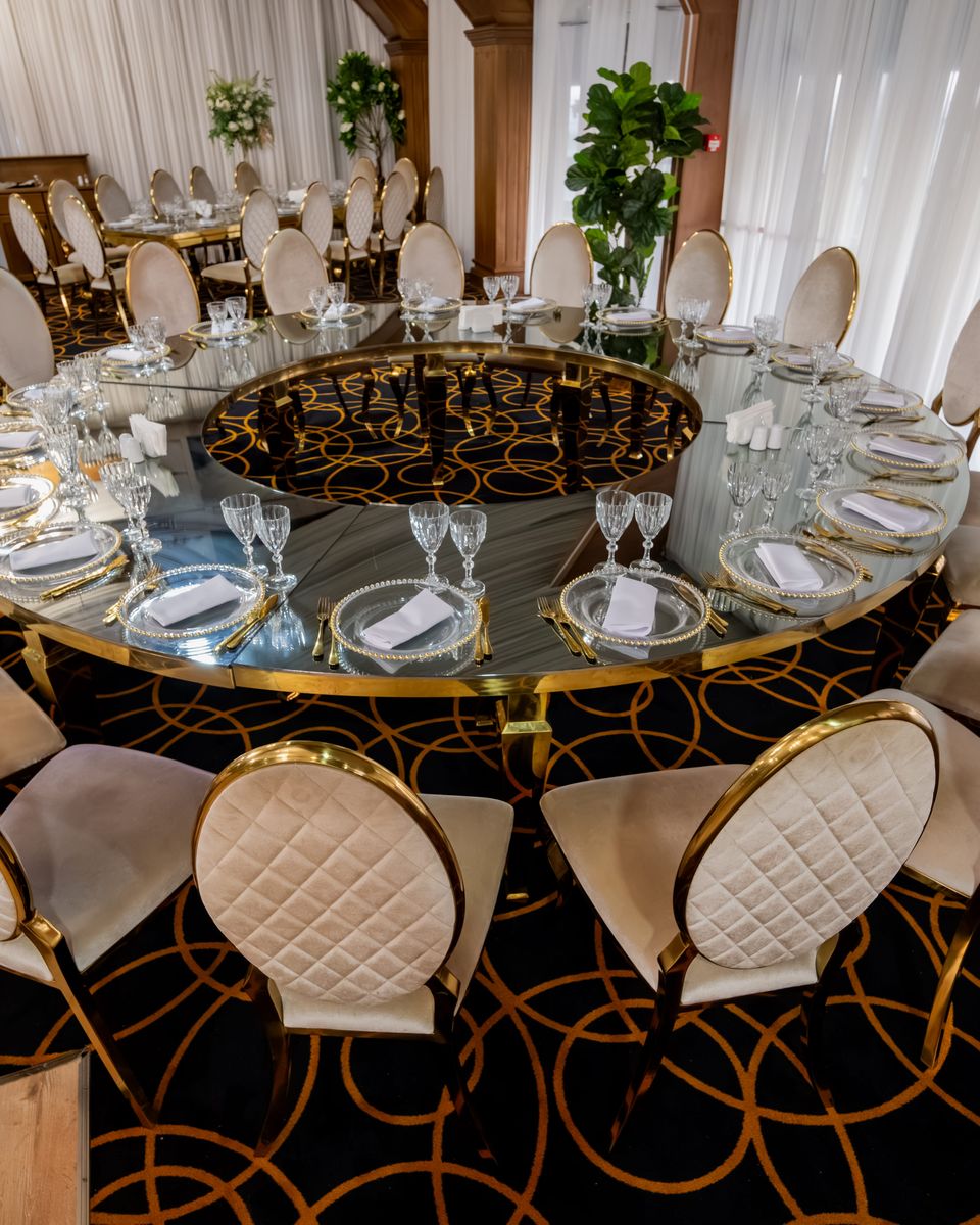 Masă rotundă cu blat de sticlă și scaune aurii, aranjată cu pahare de cristal, în Grand Event Ballroom